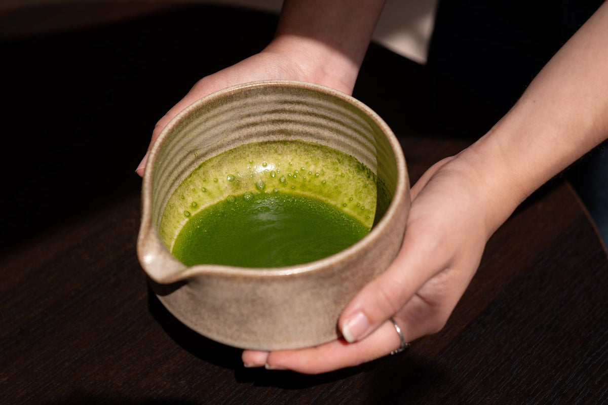 Two hands holding a bowl of whisked matcha